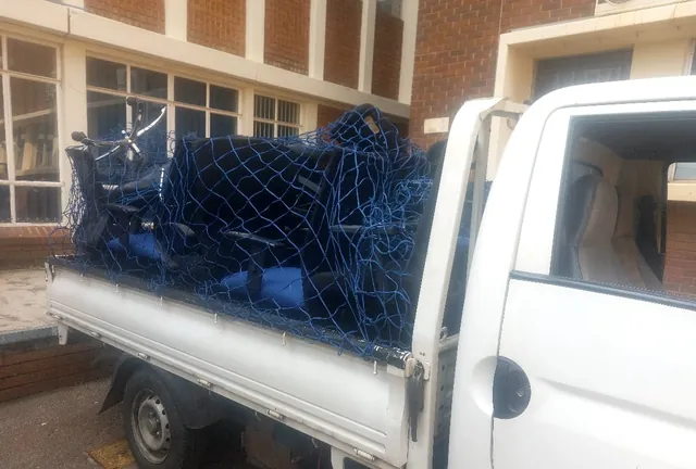 A Lewin Projects bakkie load covered and secured under a cargo net outside a brick building